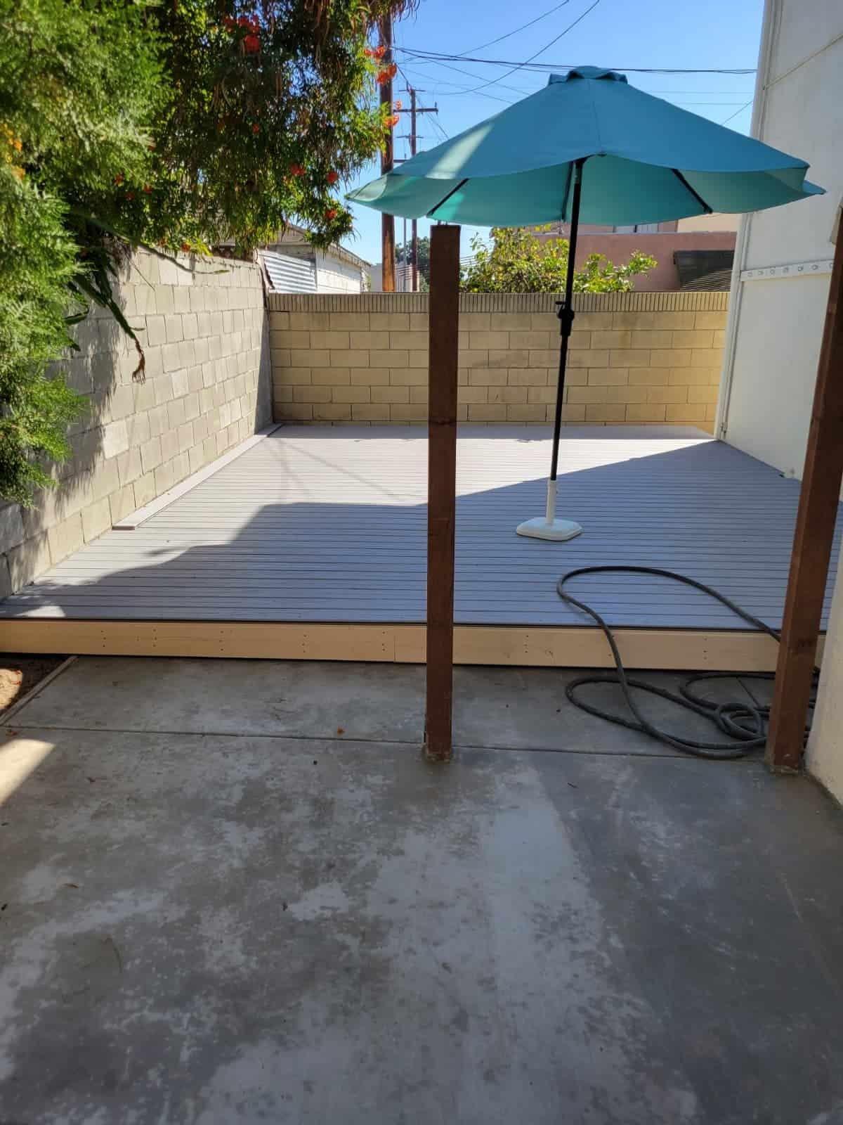 Newly installed patio deck with an outdoor umbrella, backyard patio renovation, and landscape improvement for enhanced outdoor living space.