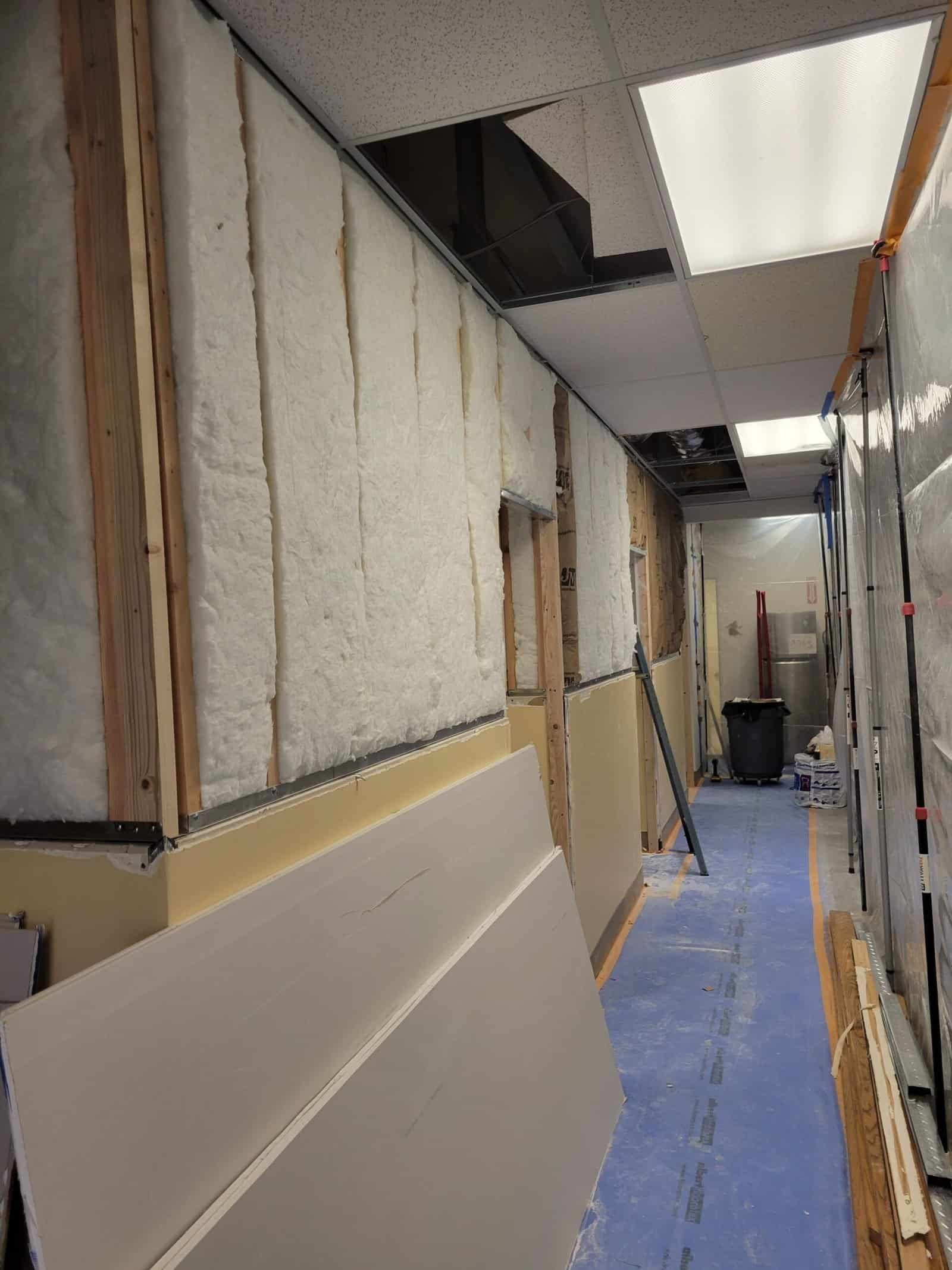 Insulation installation process with drywall panels being prepared for ceiling and wall finishing, highlighting ongoing general maintenance work in commercial or office space.