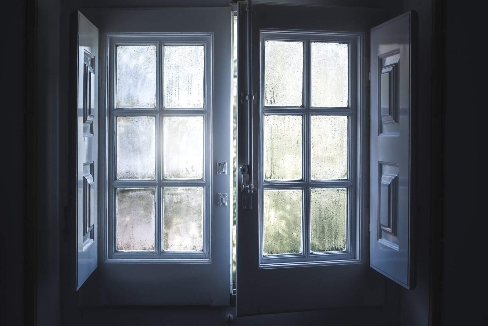 Foggy window panes with condensation and window frames in a dimly lit interior space.